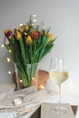Still life with a bouquet of colorful spring tulips and a glass of white wine on the work desk.