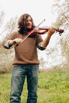 Man with long hair playing violin standing in field