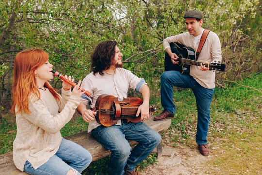 Folk music group with musical instruments discussing with each other near bench at roadside