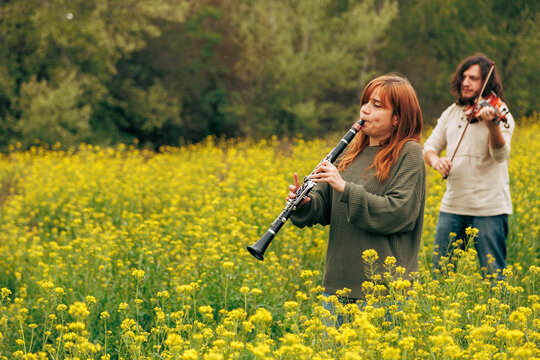 Woman practicing clarinet with man playing violin walking in flower field