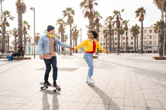 Happy couple holding hands skating together on footpath