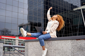 Carefree businesswoman with hand raised sitting on wall outside office building