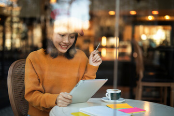 Happy woman using credit card to shopping online with tablet. Beautiful young woman drinking coffee in cafe.