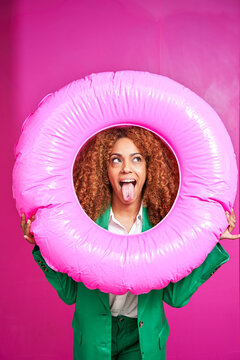 Businesswoman With Sticking Out Tongue Looking Though Inflatable Ring Against Pink Background