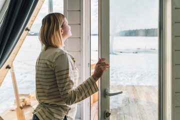 Woman breathing fresh air by glass door at home