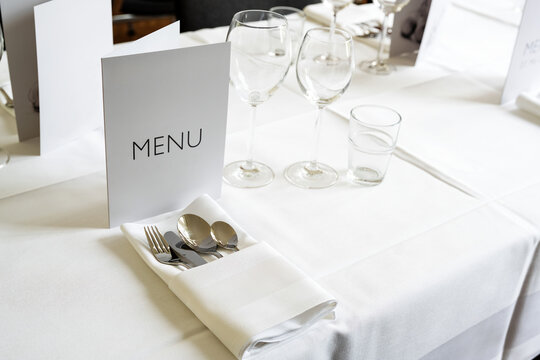 Elegant place setting with menu card, various glasses, cutlery and napkin on a table with white tablecloth for a festive dinner, copy space, selected focus