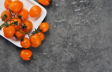 Cherry tomatoes of orange color in drops of water, layout on a gray table. Dark style, ingredients...