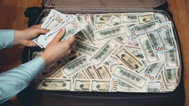 man considers the US currency over a suitcase full of money