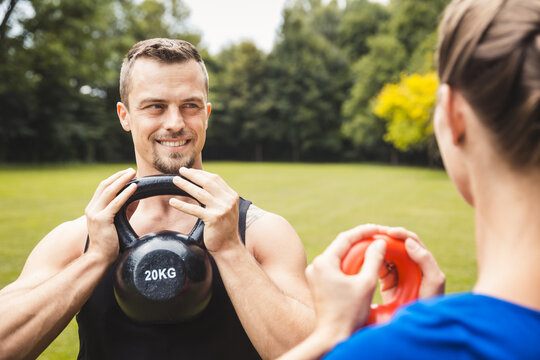 Portrait of fit and healthy handsome young male exercising in park using kettle bel with female instructor