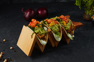 Set of delicious tacos with avocado paste on wooden rack