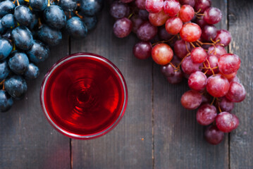 glass of red wine and grapes on black wooden table background