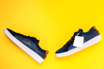 Pair of male's new sneakers made of blue leather on a yellow background. White label with copy space. Flat lay. Mock up. Side view of shoes