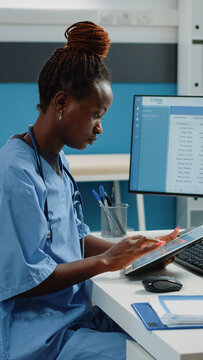African american nurse using digital tablet for treatment. Black medical assistant looking at screen of device while wearing uniform and stethoscope in doctors office for healthcare.