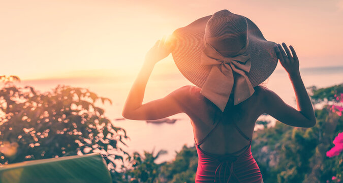 Young slim beautiful woman in bikini and hat enjoying tropical vacation with sunset sea view
