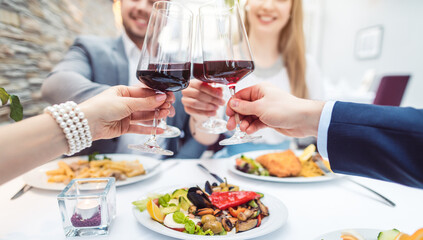 Close-up on hands of patrons in restaurant with glasses of red wine over table with food - 503419149