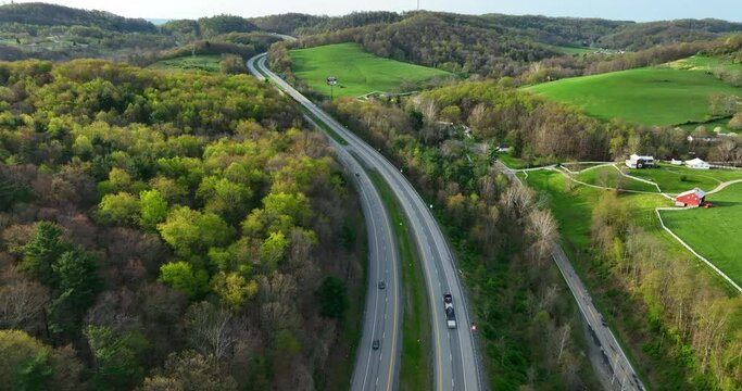 Appalachian Mountains in USA. Turnpike highway road cuts through winding hills and valleys. Interstate transportation theme. Green nature countryside aerial tracking of traffic.