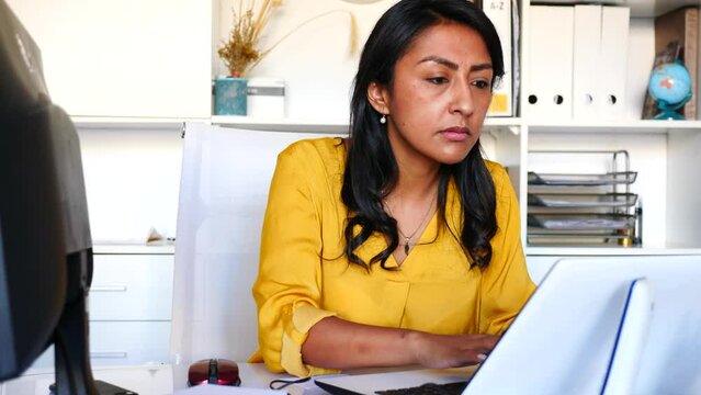 Portrait of busy latin american female office employee working at desk with computer