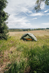 A green tent pitched on a high grass meadow. Opened tent in the mountains on a sunny day. Camping gear.