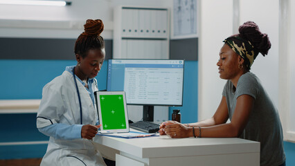 Medic pointing at tablet with green screen and talking to patient for consultation. Doctor and woman with technology looking at chroma key with isolated background and mockup template