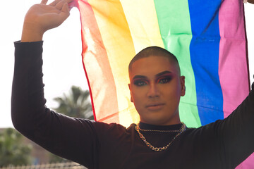 Portrait of non-binary person, young and South American, heavily make up and holding a gay pride...