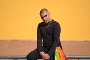 Non-binary person, young South American, heavily make up, sitting on a railing with a gay pride...
