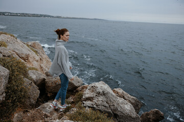 beautiful woman in a gray sweater stands on a rocky shore nature Relaxation concept