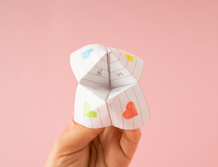Paper origami fortune teller in hand against pink background. Minimal concept.