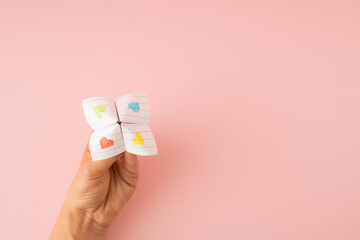 Paper origami fortune teller in left hand on pink background. Minimal concept.