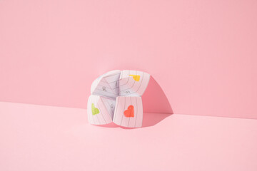 Paper origami fortune teller leaning against pink background. Minimal concept.