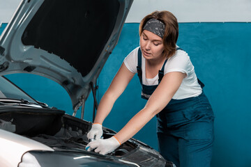 Young woman mechanic in coveralls and gloves repairs the engine. Mock up with copy space. The...