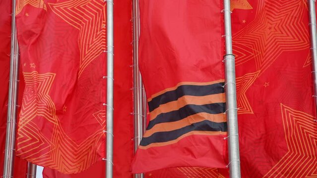 Group of red flags with george ribbons and stars swings on flagpoles. Overcast sky in the background. 4K resolution real time video. Russian Victory day holiday theme.