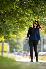 Blind woman walking on city streets, using her white cane to navigate the urban space better and to get to her destination safely