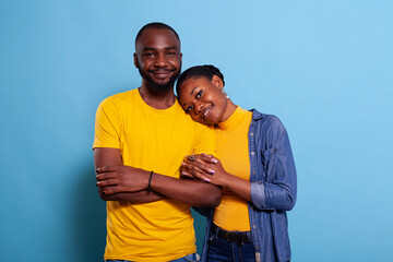 Cheerful couple holding hands and bonding in studio, showing affection with romantic embrace. Positive people in love expressing gratitude, cuddling together over blue background.