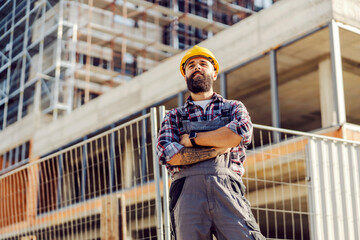 Low angle view of a proud worker at construction site. - obrazy, fototapety, plakaty