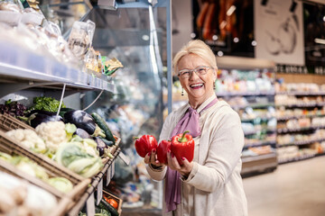 A happy senior woman buying peppers at supermarket.