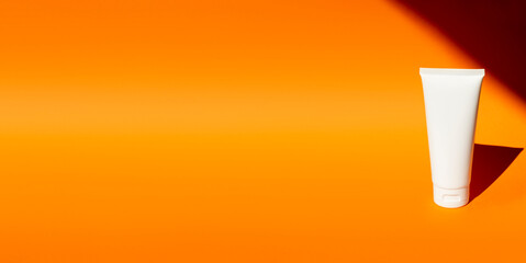 Plastic white tube for cream or lotion. Skin care or sunscreen cosmetic on orange background with plant shadows. Beauty concept for face care