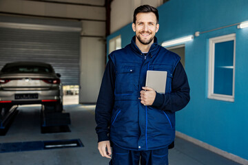 A successful car mechanic's shop worker holding tablet in hands and smiling at the camera.