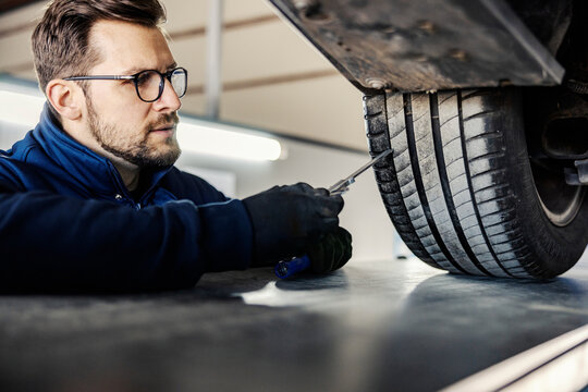 A car mechanic's shop worker checking on car tire in garage.