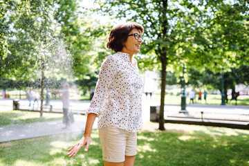 Joyful and smiling Asian woman in eyeglasses jumping and playing in fountain. Summer holiday vacation, moisturizing time