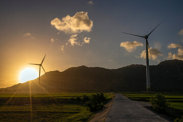 Wind turbines farm in a big green field at beautiful sunset generating electricity. Clean alternative energy concept to reduce global warming and climate change for sustainable development.
