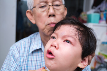 Portrait 1-2 year old Asian boy is coughing, child cries with red and swollen eyes due to injury in middle of his forehead, baby parents are comforting beside him. Home accident concept.