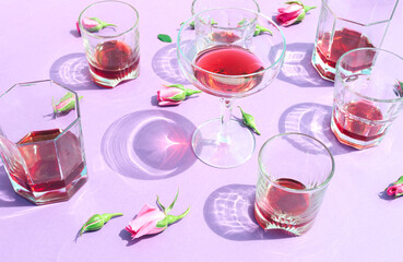 Glasses of wine and roses flower on a purple background. Sunny aesthetic romantic party drink concept. 