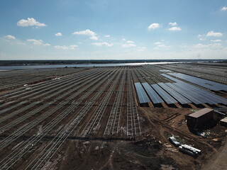 Aerial view of solar power plant under construction on a dirt field. Assembling of electric panels...