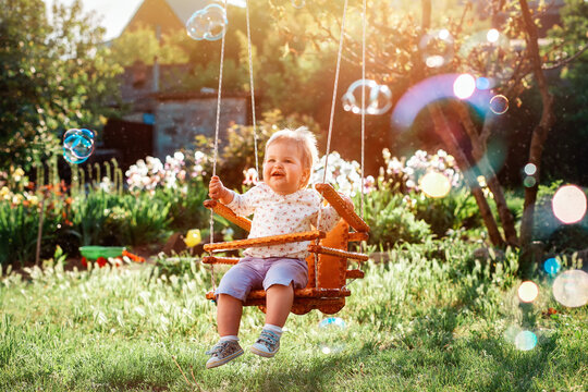 Happy baby girl having fun on a swing. Sunny playground in a kindergarten. Soap bubbles flying around. The concept of the International Children's Day