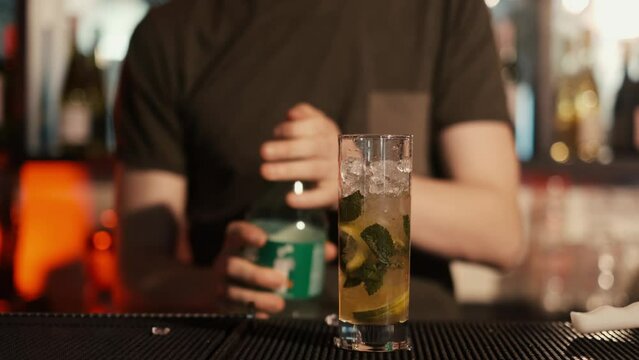 A professional bartender is preparing an alcoholic cocktail with ice cubes to customers at the bar or disco club.