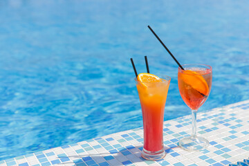 Two citrus cocktails in the summer by the pool against the backdrop of blue water, copyspace