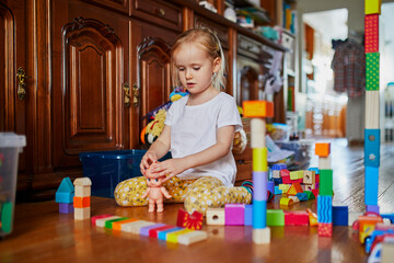 Adorable prechooler girl sitting on the floor and playing with colorful construction blocks