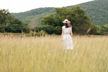 Summertime. Woman in a straw hat and dress is walking in a clearing. Back view. Copy space. The concept of psychology