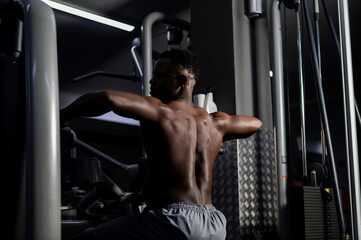 Fototapeta na wymiar Shirtless african american man doing back exercises on a machine in the gym.