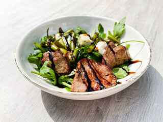Beef roasted meat with balsamic vinegar, green beans, and arugula on a white plate. Plate. Beef. Cooked. Steak. Grilled. Delicious. Dish. Roast. Lunch. Roasted. Salad. Gourmet. Organic